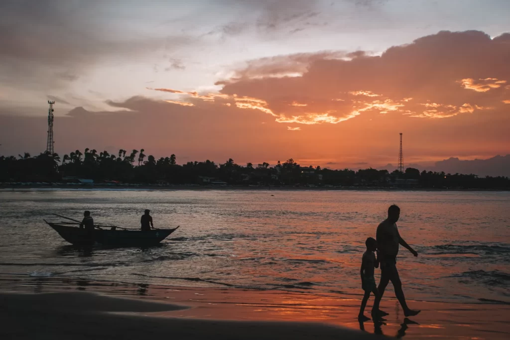 A man with his child walks past a fishing boat at sunset on Arugam Bay beach