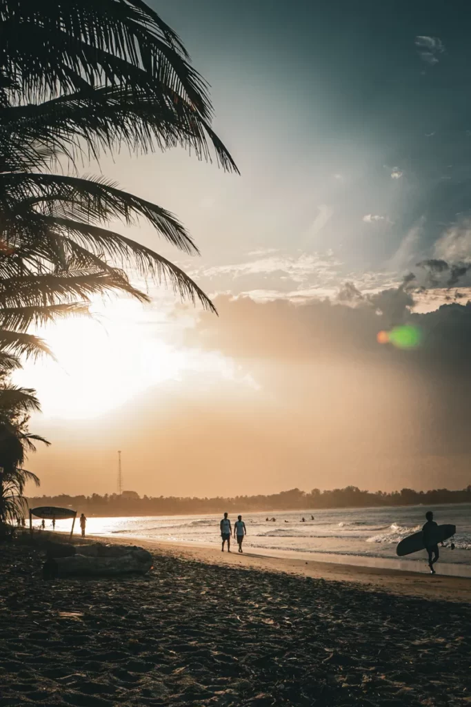 Surfers walk down the beach at sunset on Arugam Bay Beach