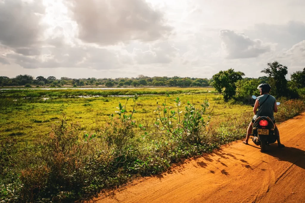 A man sits on a motorbike looking at a lake on the way to Peanut Farm Beach