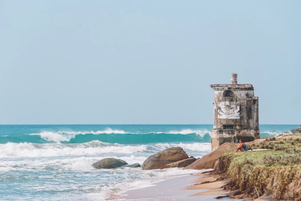 full-width-mobile A girl sits in front of the lighthouse looking at the surf at the beach