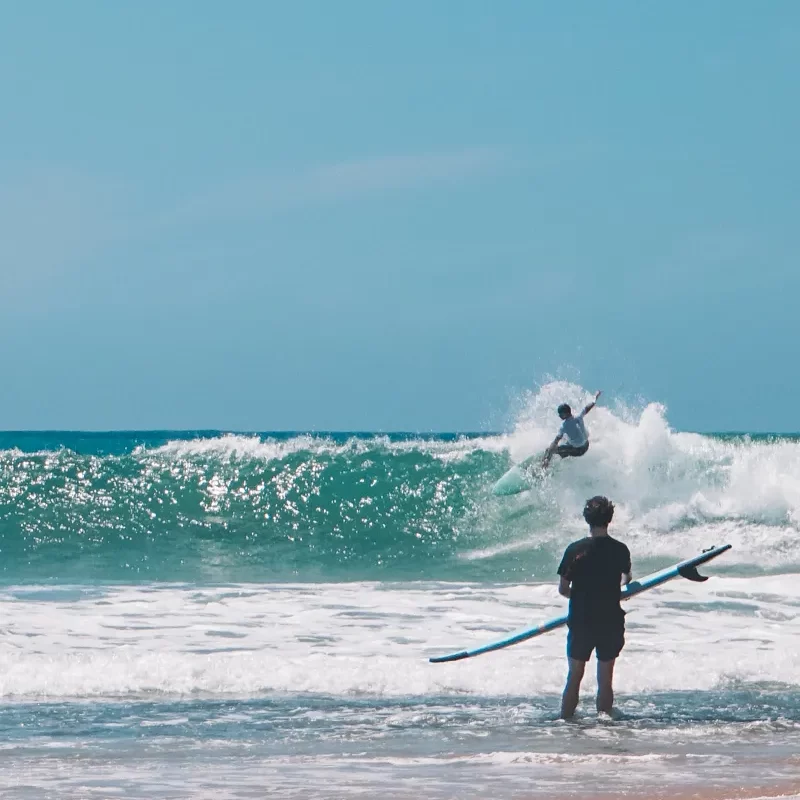 A surfer does a cut back at Main Point in Arugam Bay whilst a beginner watches him from the beach