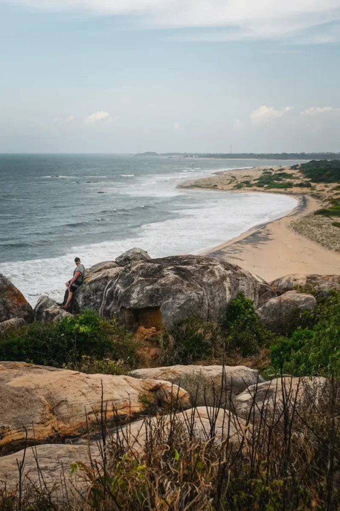 A man sits on some boulders looking at the coastline on the top of Elephant Rock