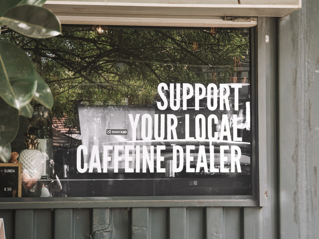 A window sign saying "Support your local caffeine dealer" on the side of Kaffi in Arugam Bay