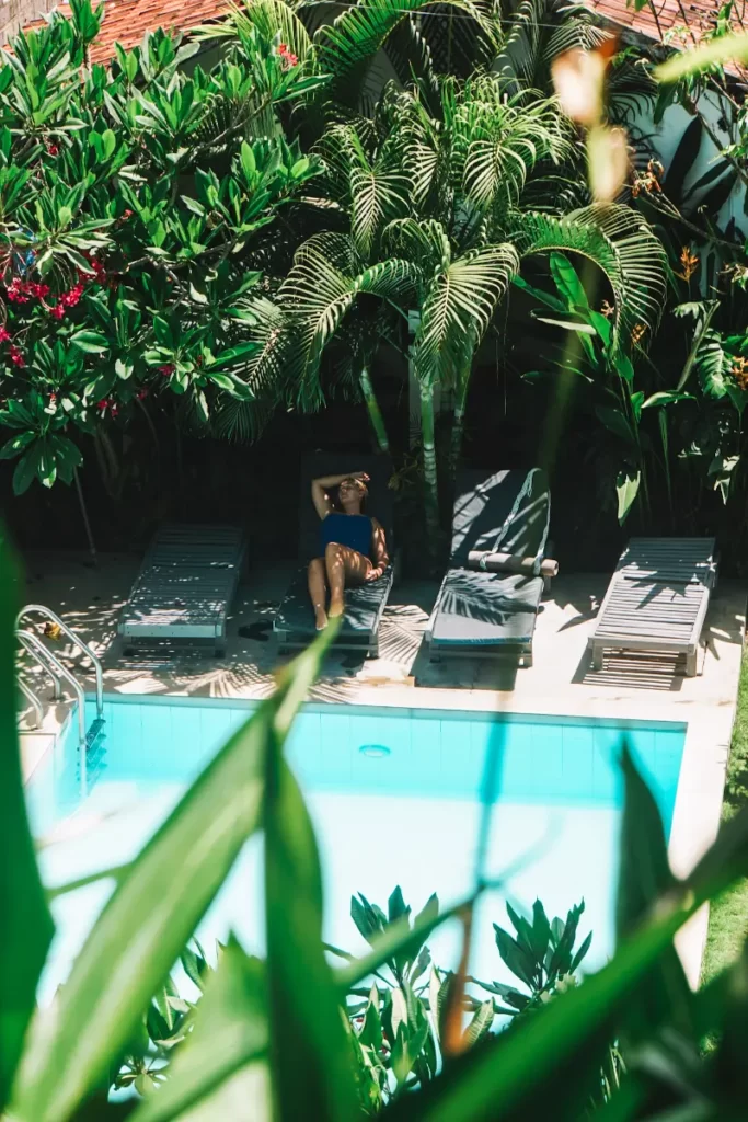 A girl lays next to a pool with palm trees and bushes all around her in Surf Gangs Arugam Bay