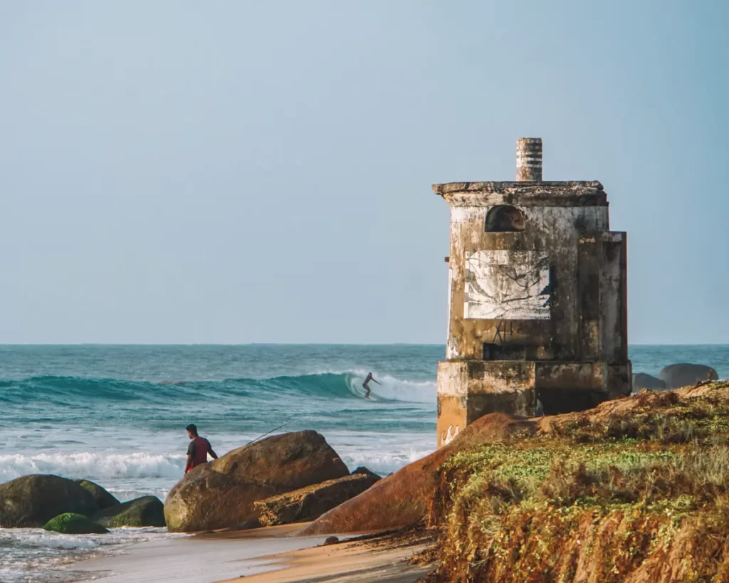 A surfer on a wave behind the lighthouse near sangamankanda Point, Komari