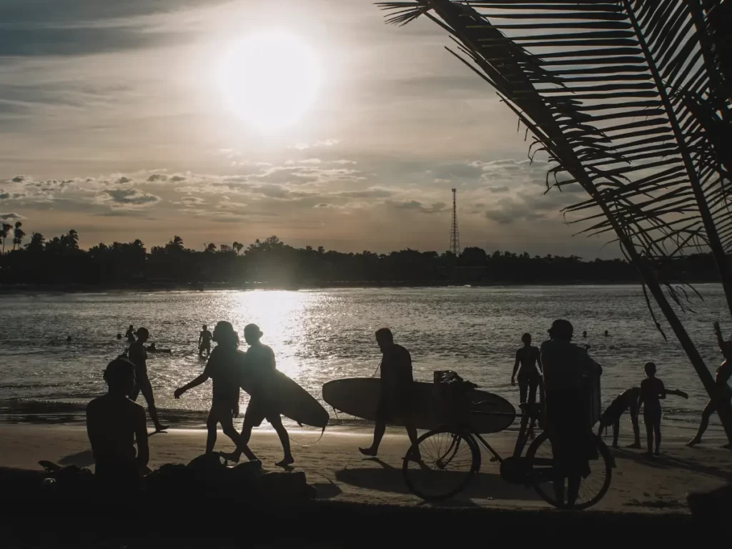 Surfers walk down the beach at sunset in Arugam Bay