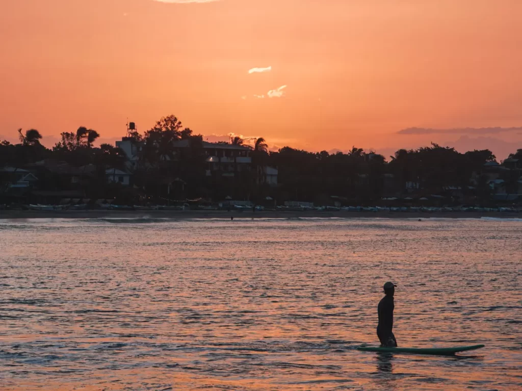 A surfer walking his board in the water at sunset in Arugam Bay