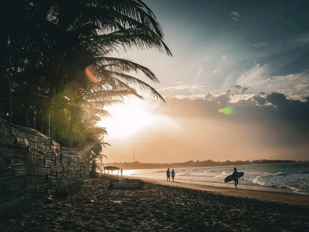 Surfers walk down the beach at dusk to Main Point in Arugam Bay