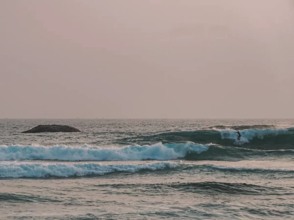 A man drops into a wave with The Rock Kabalana in the background