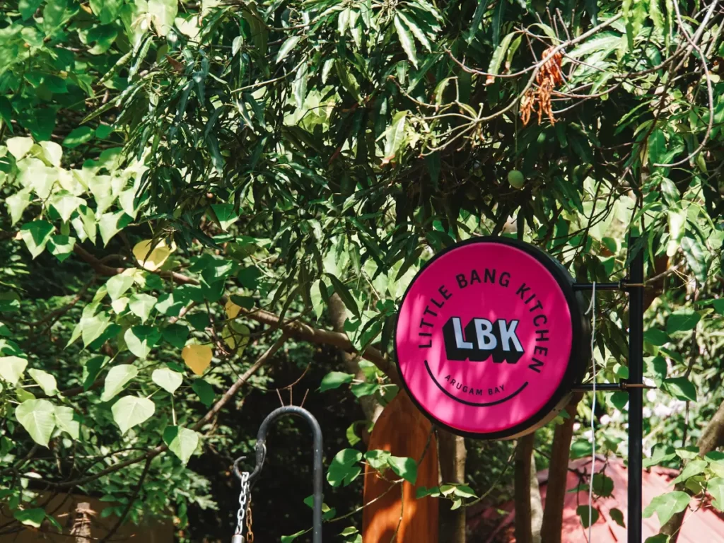 The pink Little Bang Kitchen sign against the backdrop of the restaurants jungle trees