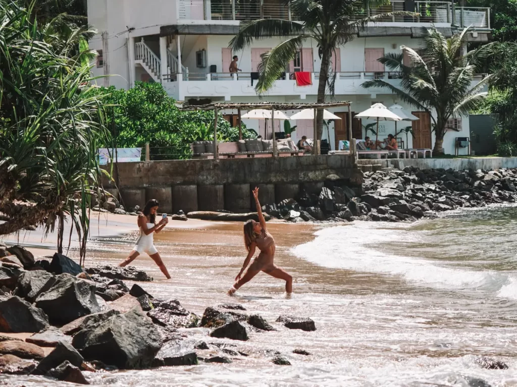 Two girls do Yoga on Ahangama Bay Beach with the Soul and Surf hotel in the bakground