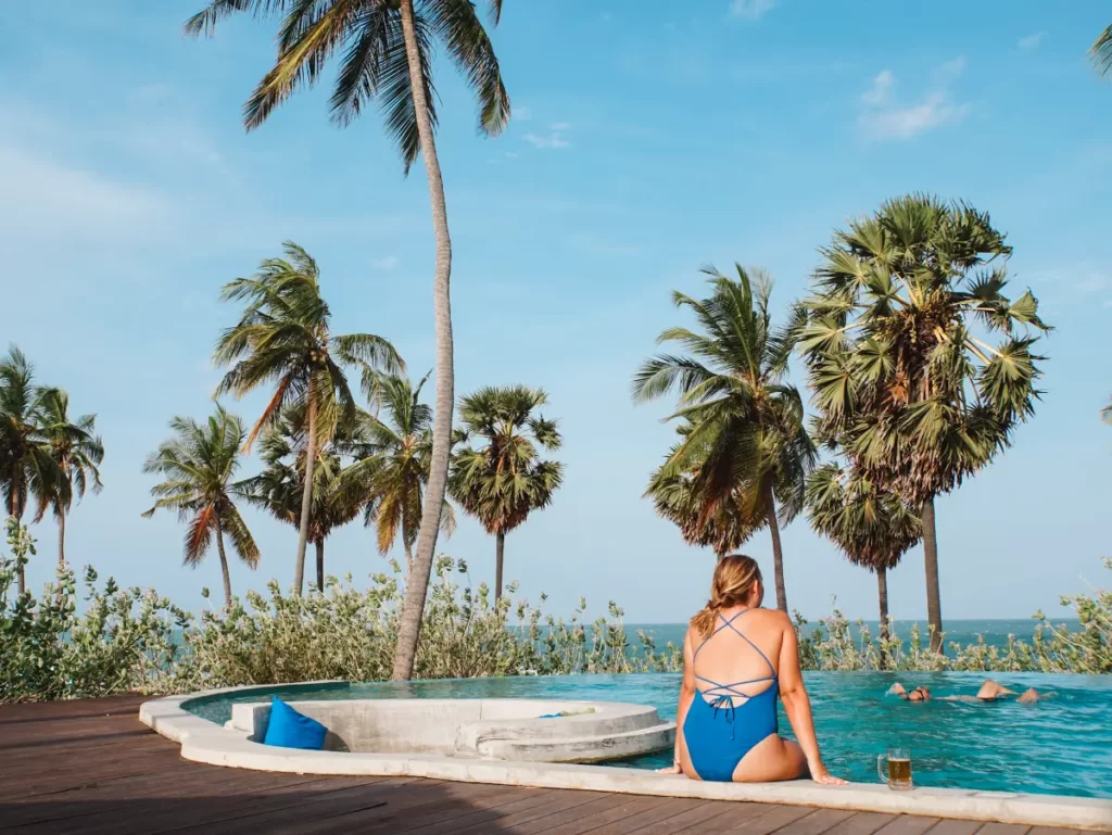 A girl sits on the edge of the pool with a beers at Jetwing Surf