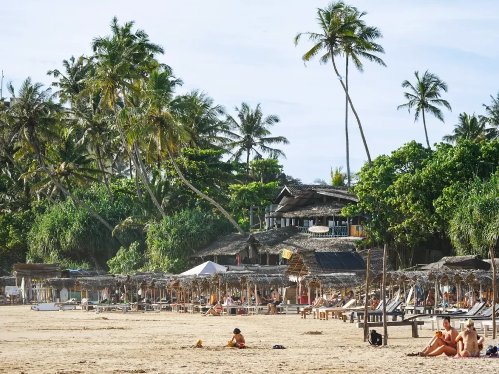 A child plays in the sand at Kabalana beach whilst people sit on the sunlougers in the background