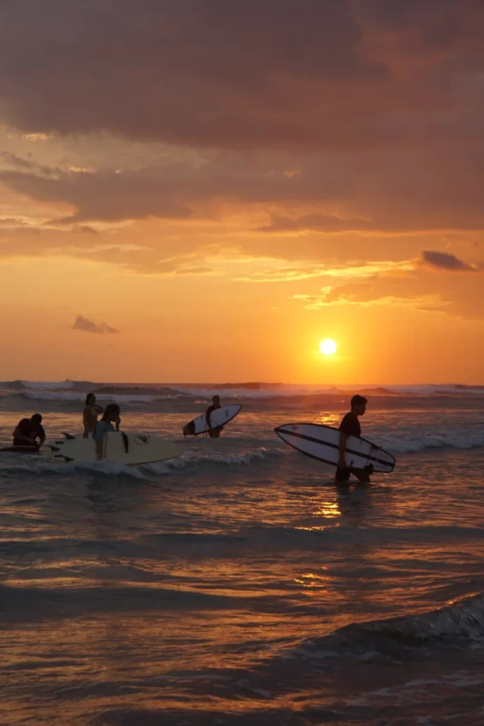 Surfers walking out of the ocean at sunset at Kabalana beach