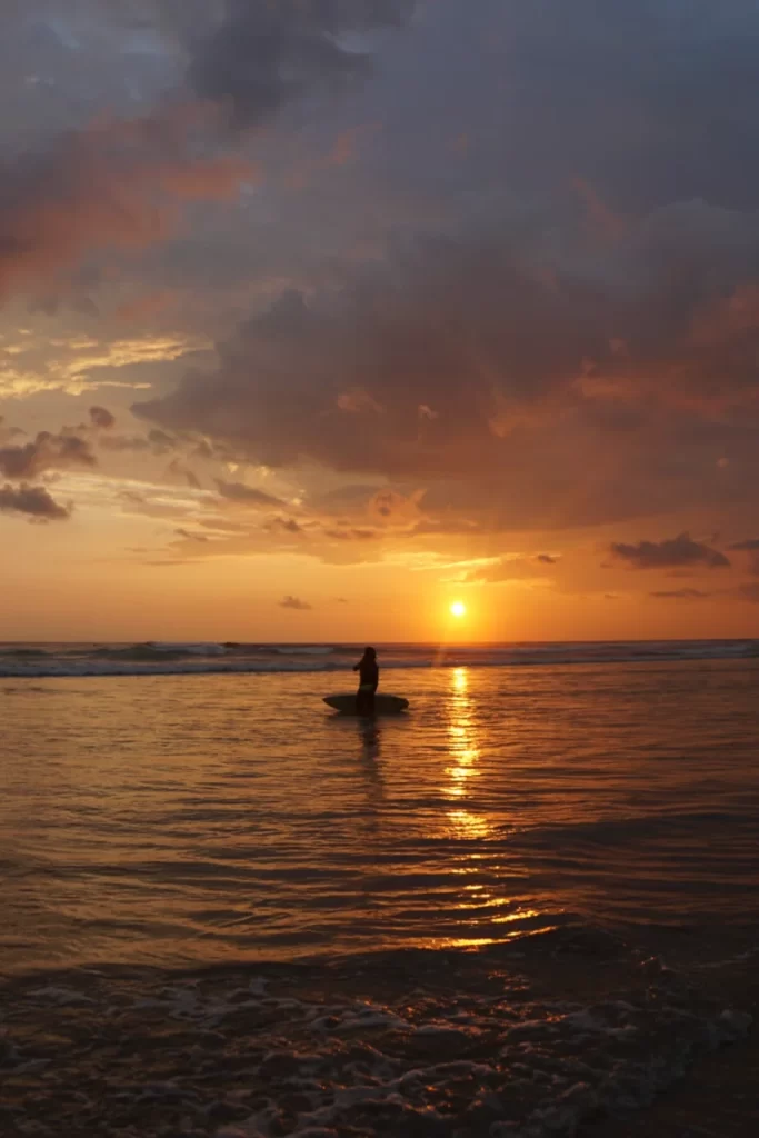 A surfer in the ocean at sunset in Ahangama