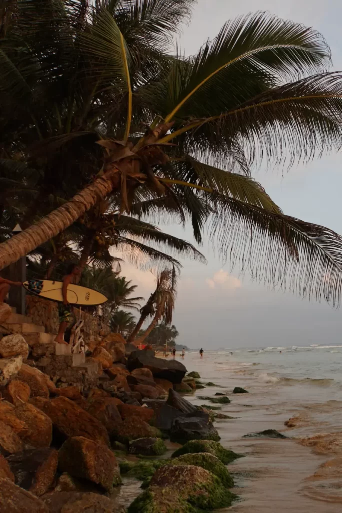 A surfer standing on the rocks at dusk at Kabalana Beach