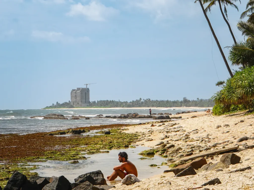 A man sits in a rock pool on a deserted beach in Madiha