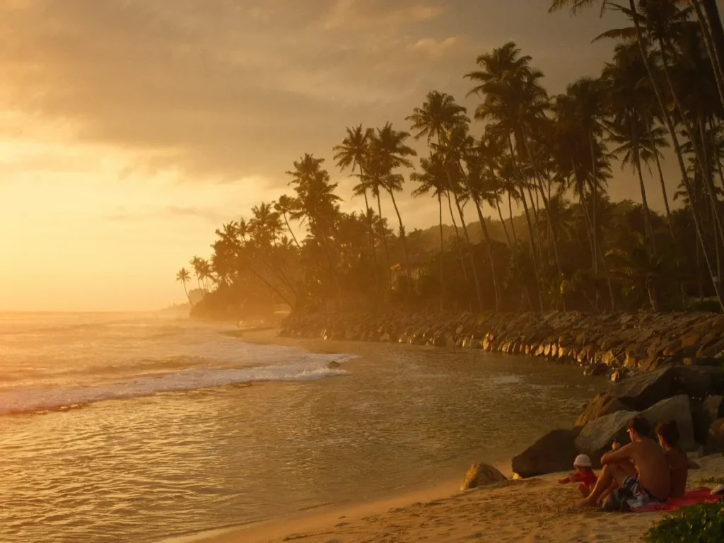 Two people sit on Madiha Beach at sunset with a misty background down the coast