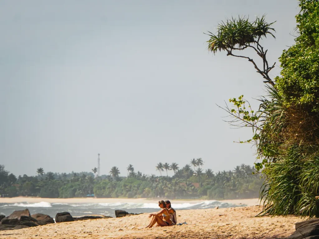 Two girls sit on an untouched deserted beach in Madiha