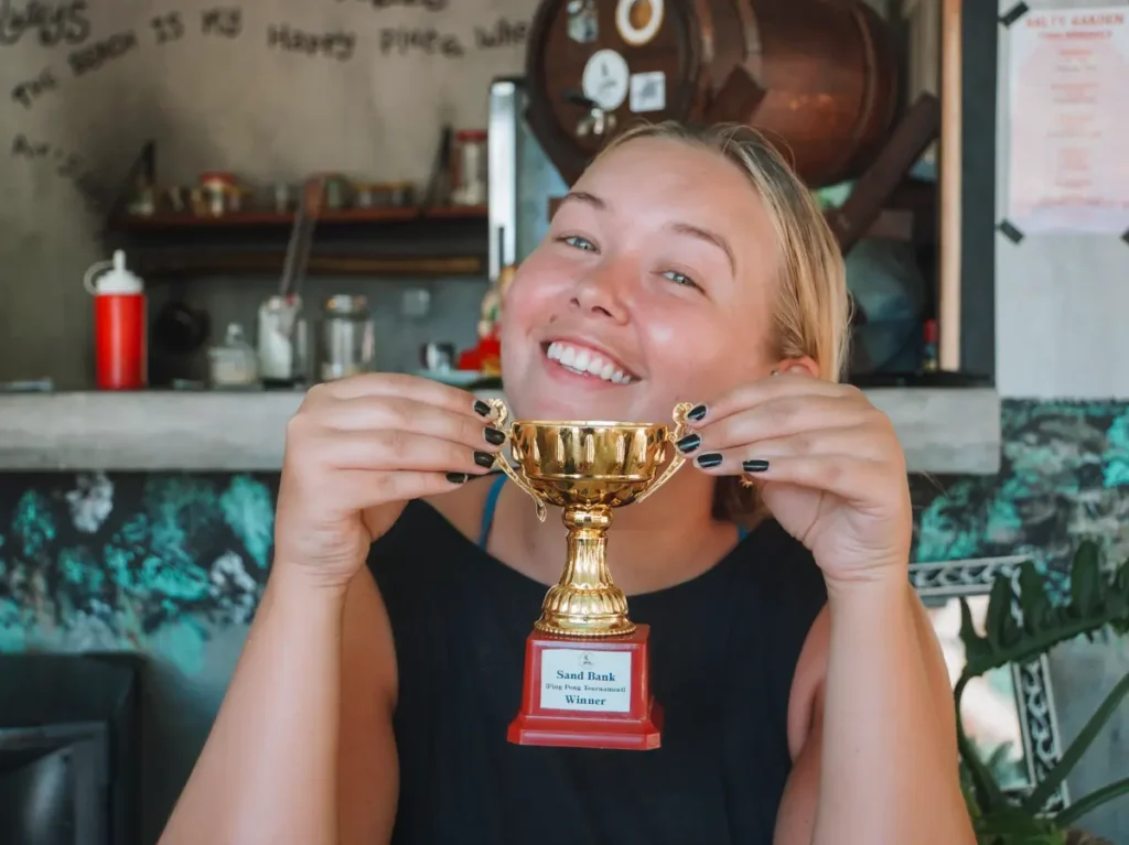 A girl lifts up the Sand Bank ping pong trophy