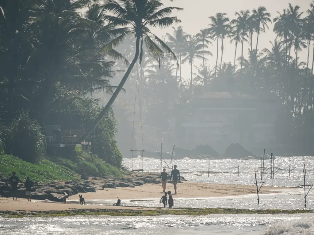 Two people walk down Ahangama Beach in the morning whilst kids play in the ocean