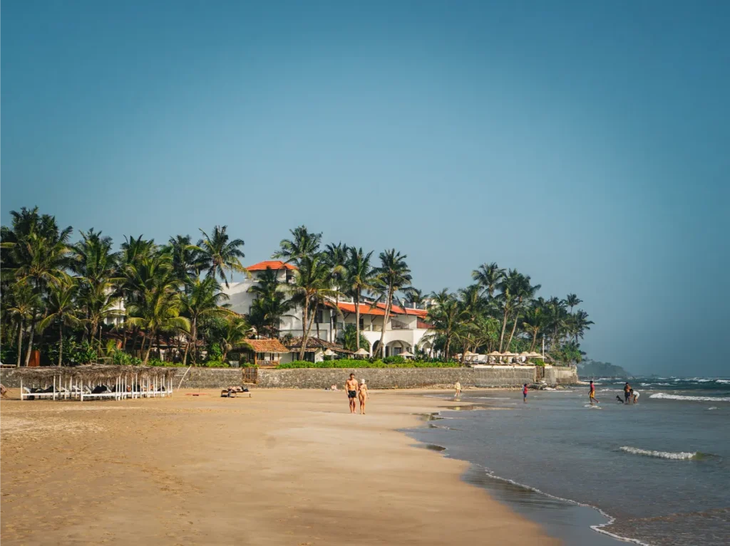 Two people walk along Kabalana beach with Mosvold Villa in the background