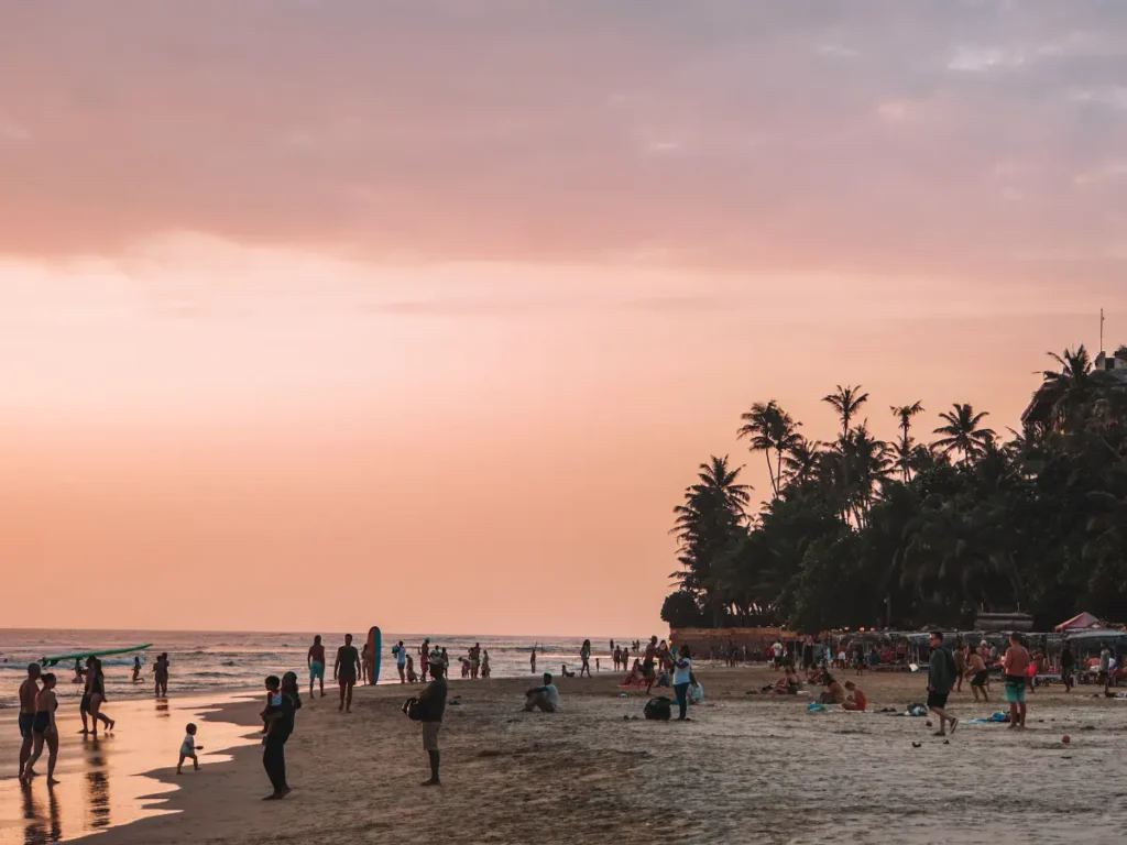 Lots of people standing on the shoreline of Kabalana beach with a pink sky at sunset