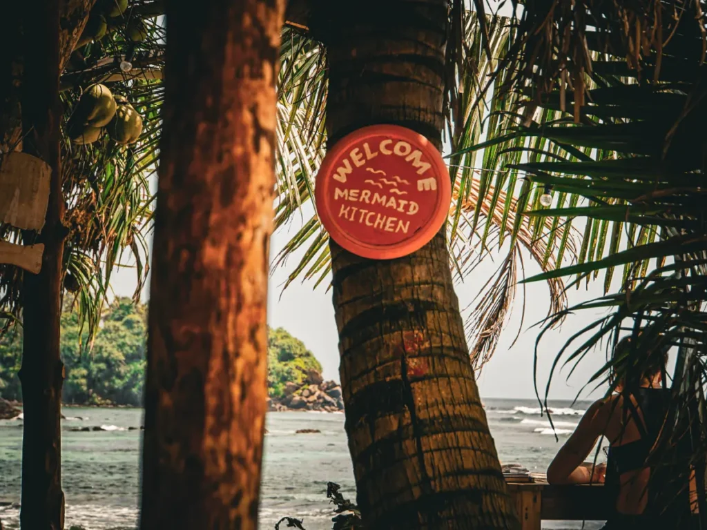 The Mermaid Kitchen's sign painted on an old clay pot and hung from a palm tree