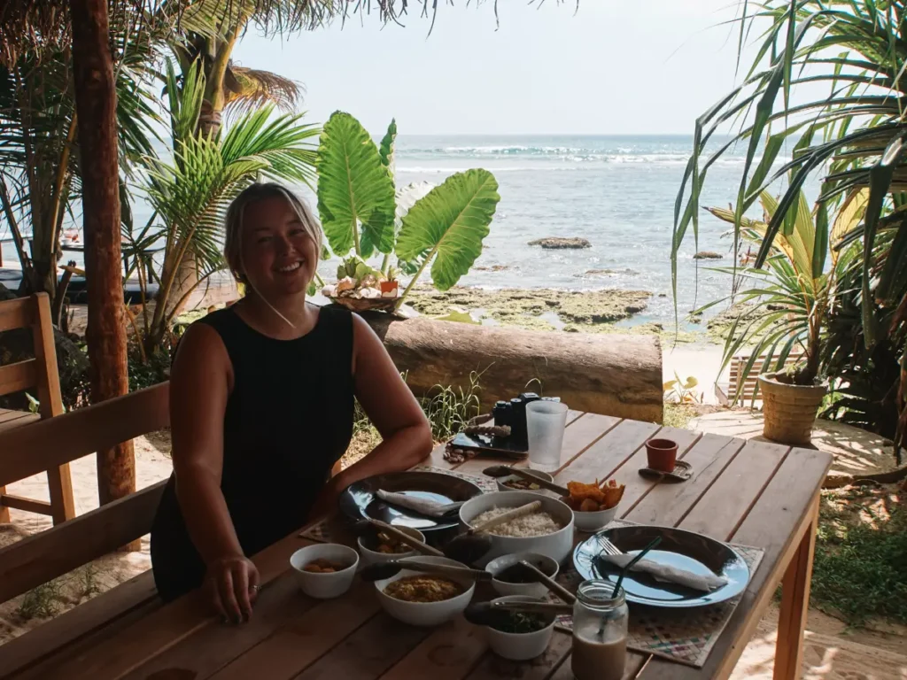 A girl sits on a table with a rice and curry at Mermaids Kitchen with a view out to the ocean