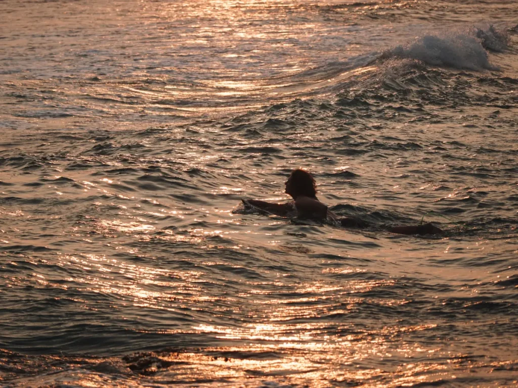 A man paddling out to Devils Rock surf spot at sunset