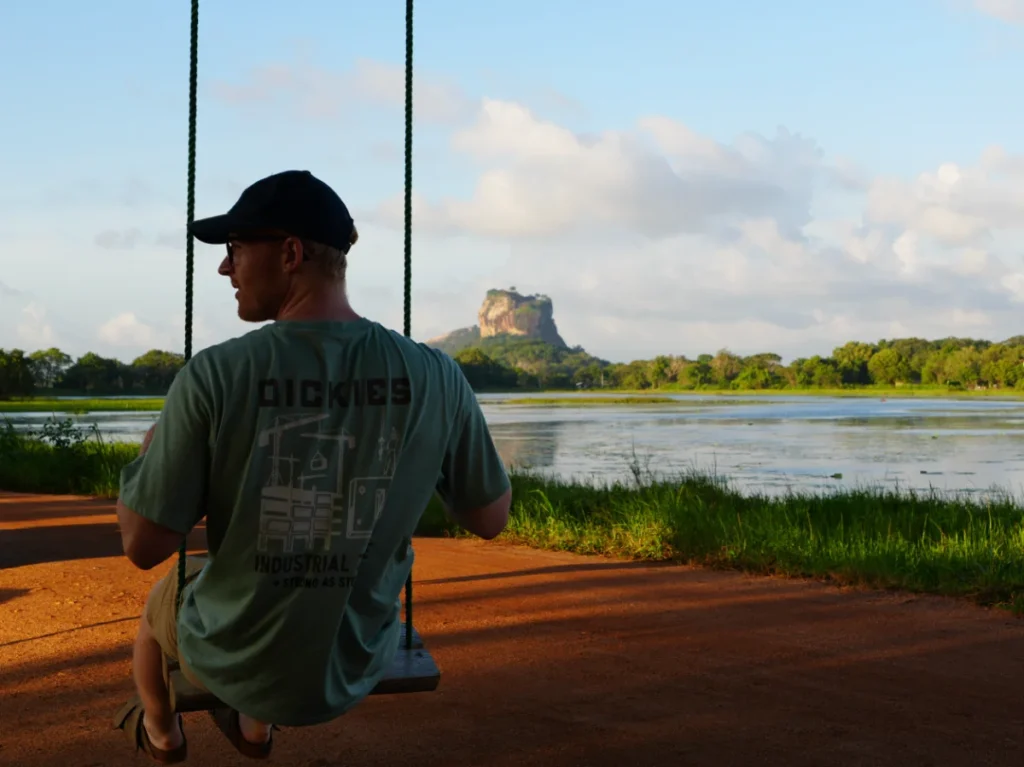 A man sits on a swing with Lion's Rock in the background
