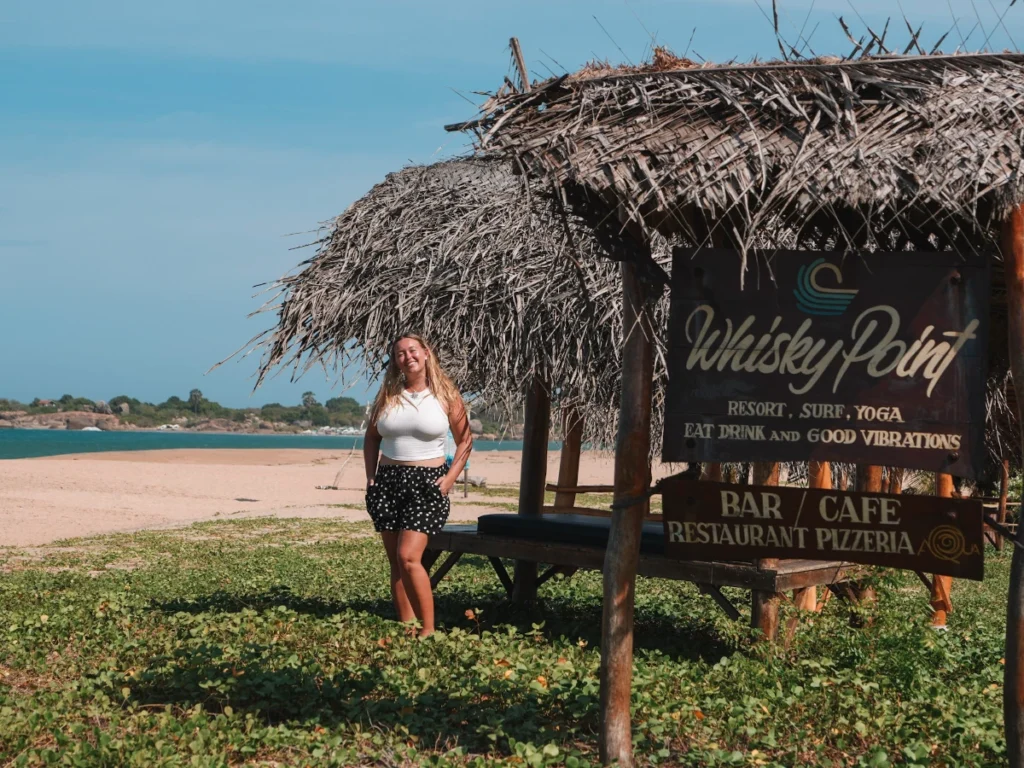 A girl stands by the Whiskey Point Resort Sign in Arugam Bay